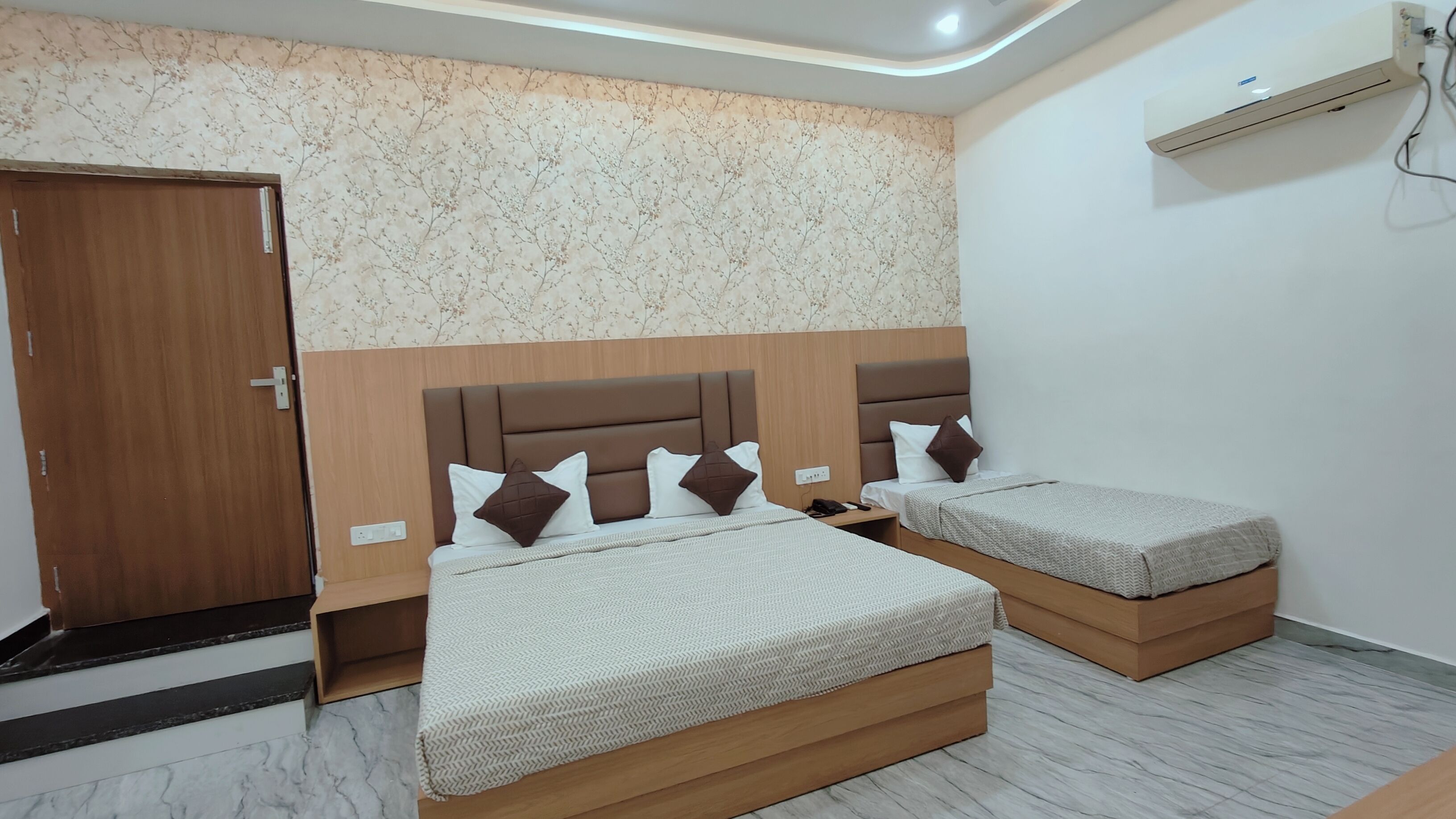 A hotel room with two beds, a wooden wardrobe, a marble floor, and a floral wallpaper.