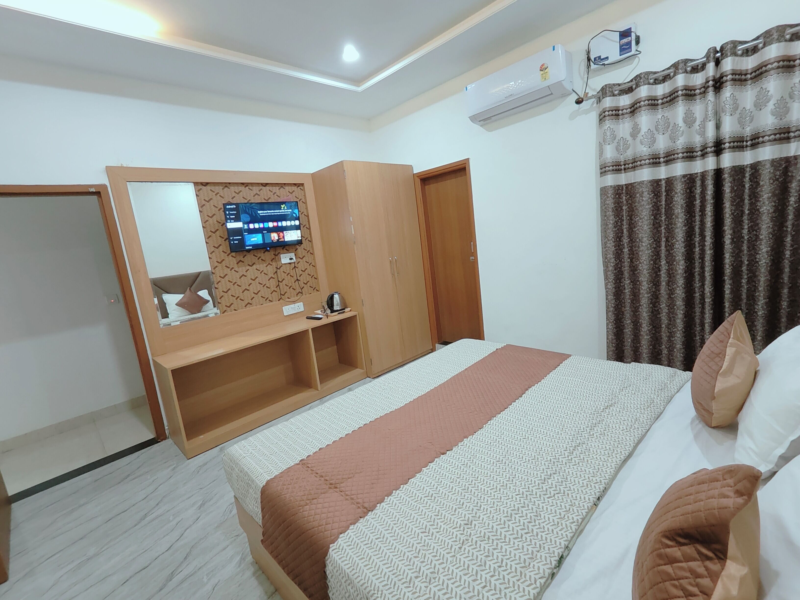 A hotel room with a bed, a desk, a wardrobe, an air conditioning unit, and a television.