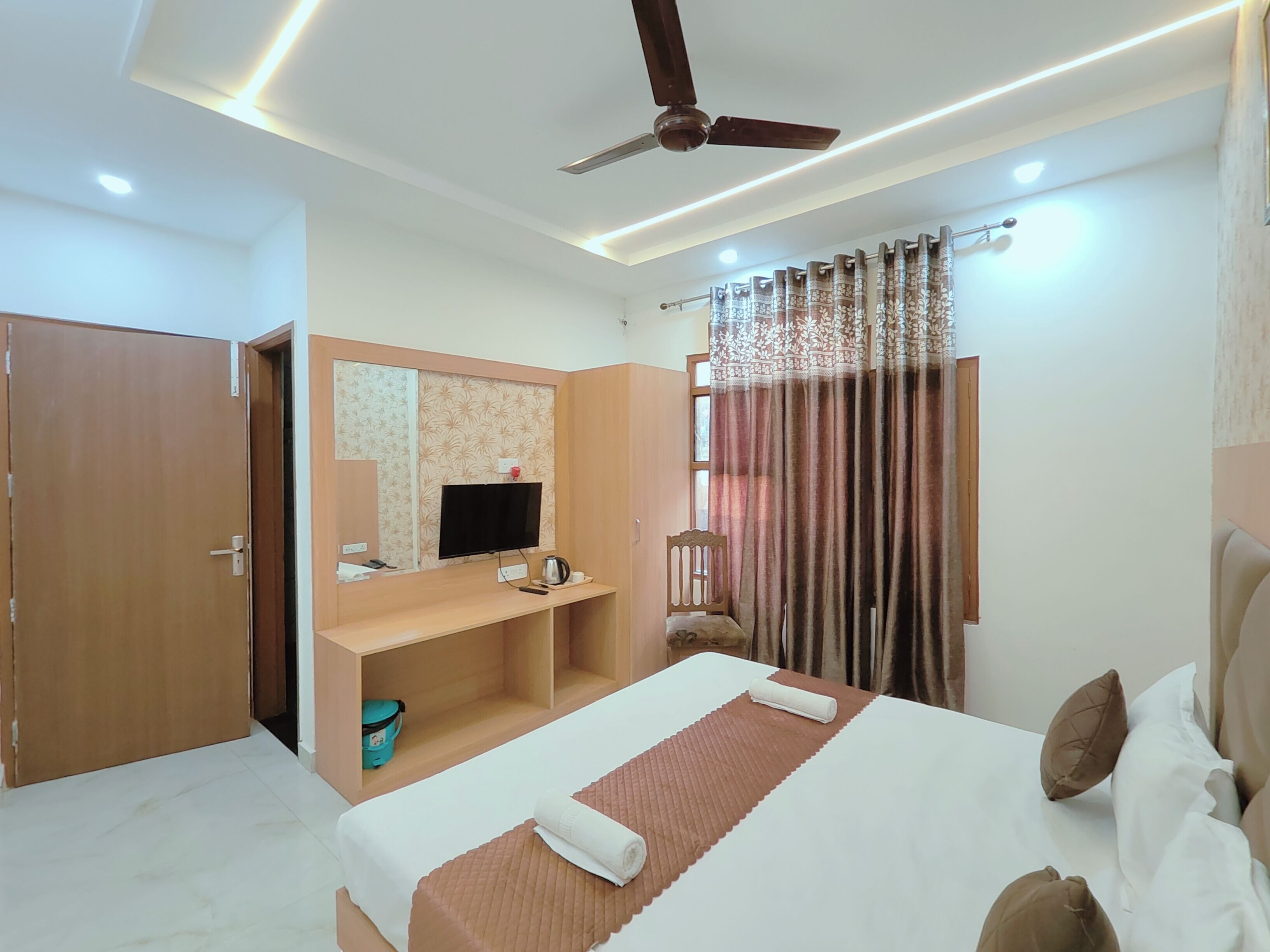 A hotel room with a bed, a TV, a desk, and a ceiling fan.