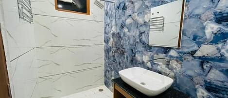 A bathroom with a white sink, marble walls, and a shower area.