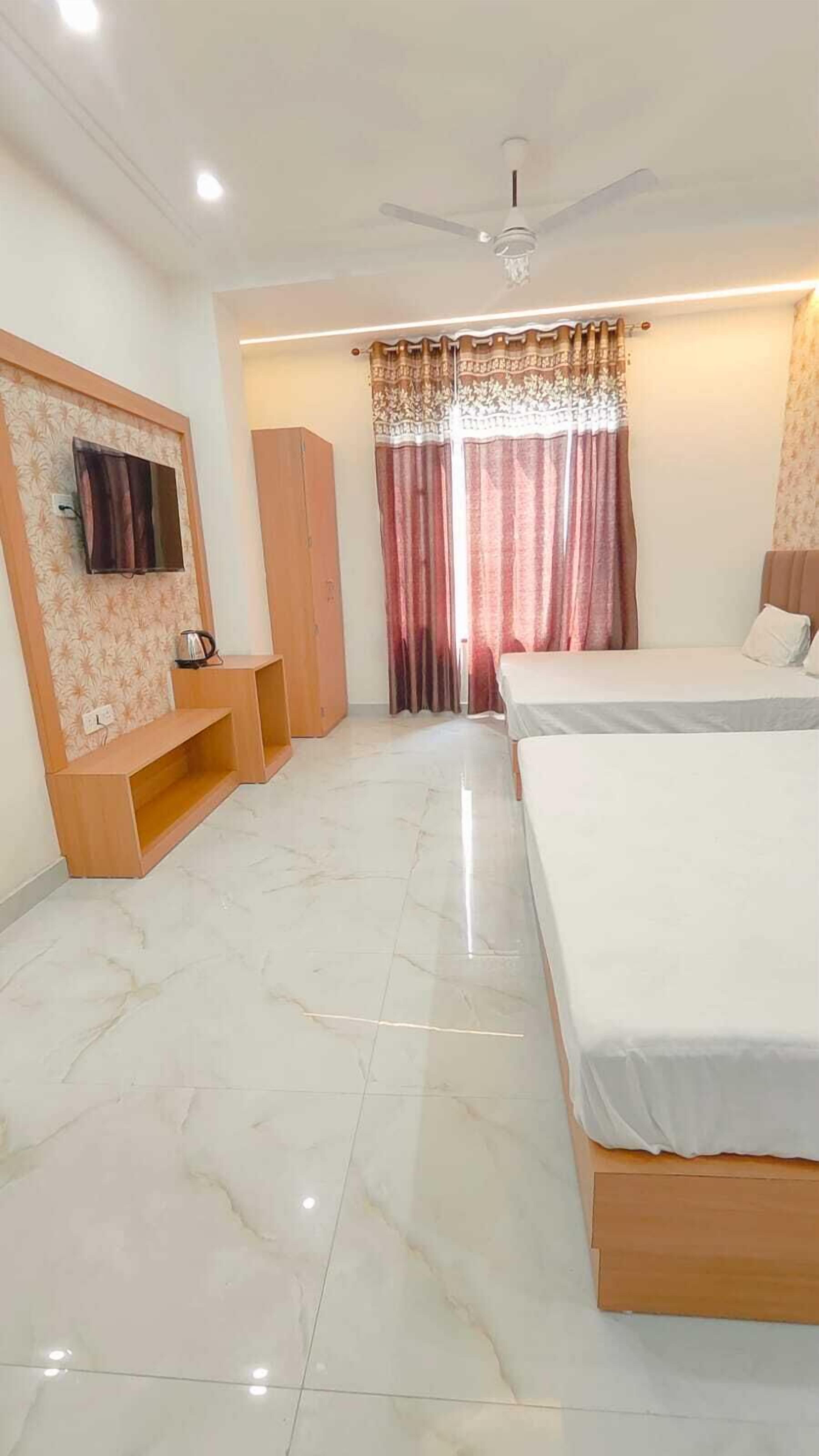 Un dormitorio con dos camas, un ventilador de techo, un televisor montado en la pared y una ventana con cortinas.