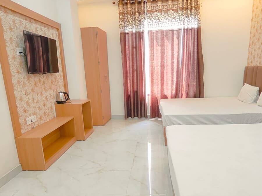 Un dormitorio con dos camas, un ventilador de techo, un televisor montado en la pared y una ventana con cortinas.