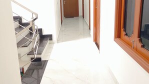 A hallway with a marble floor, wooden doors, and a staircase with metal railings. - Hotel Pilgrim Near Golden Temple (Amritsar)