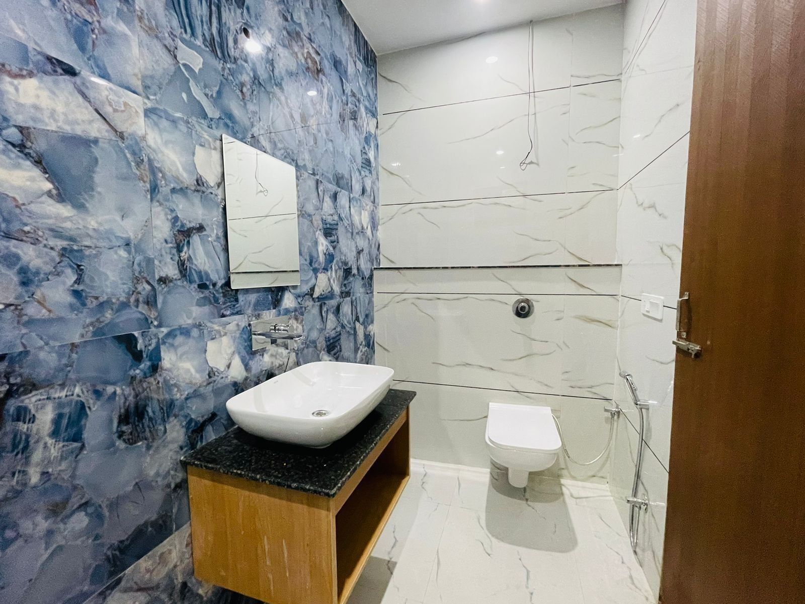 A bathroom with a marble wall, a sink, a toilet, and a shower.