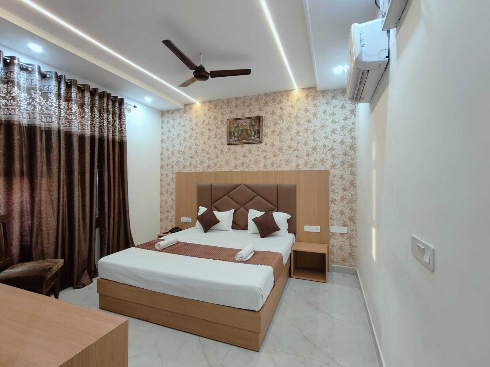 A hotel room with a large bed, a ceiling fan, an air conditioning unit, a bedside table, and a nightstand.