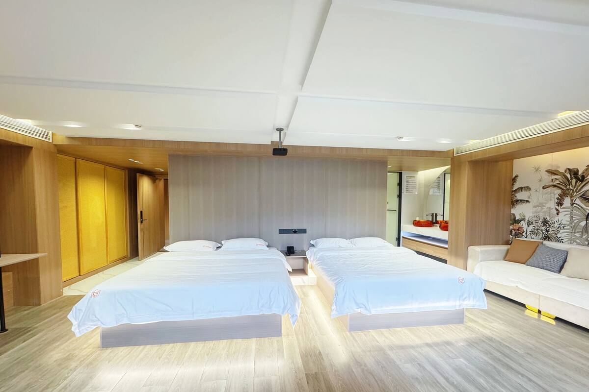 Una habitación de hotel moderna con dos camas, un sofá, suelo de madera y un mural grande en la pared.