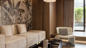 A modern living room with a beige sofa, a white armchair, a black floor lamp, and a wall mural of tropical plants. - Leshan Manfu Hotel (Leshan)