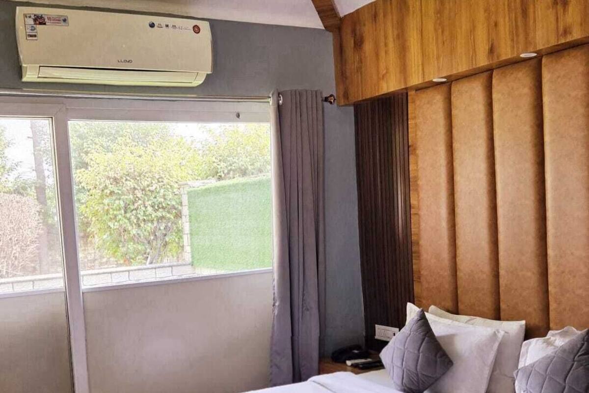 Un dormitorio con cama, ventana, cortinas, unidad de aire acondicionado y cabecera de madera.