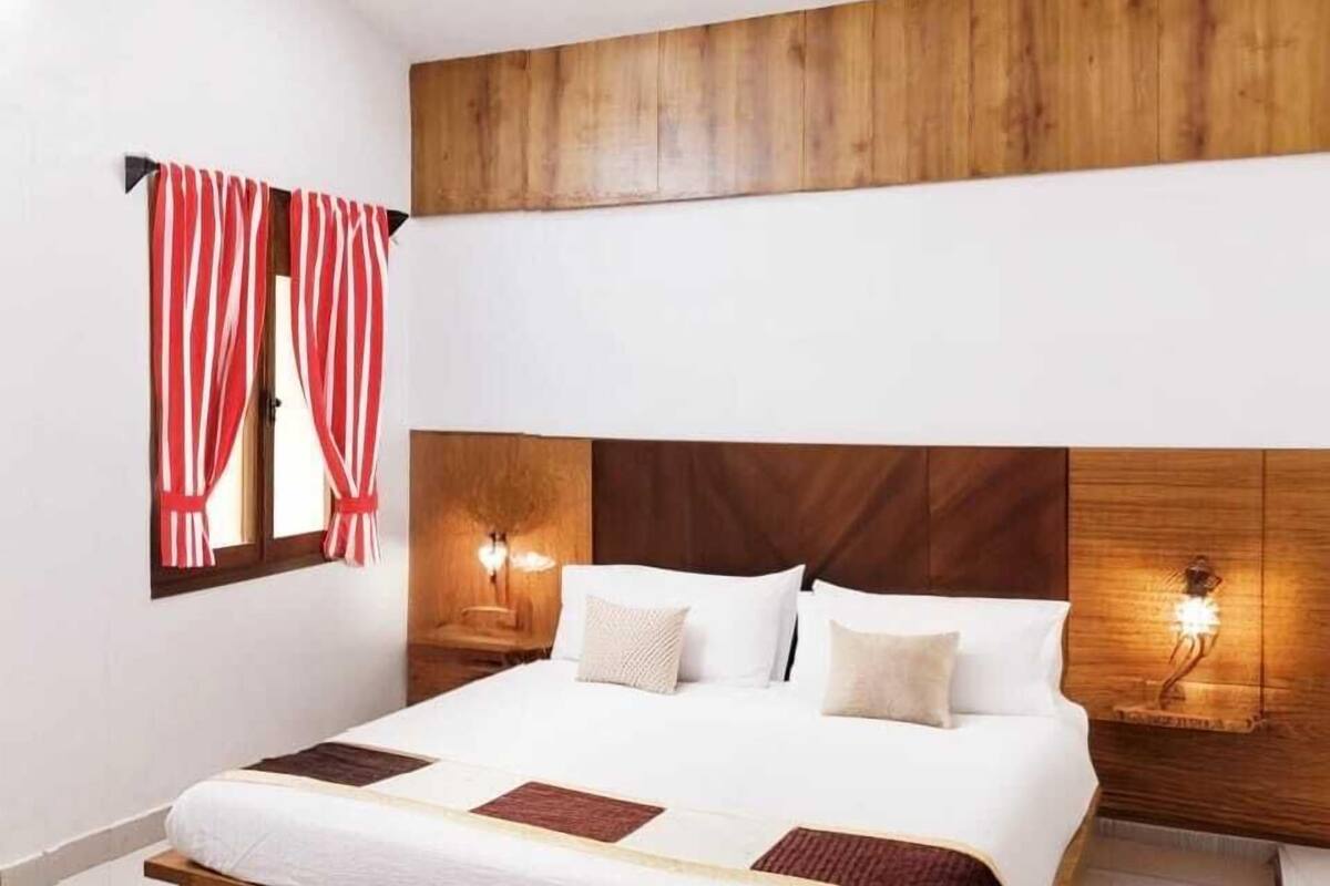 Un dormitorio con cabecera de madera, cama con ropa blanca, dos lámparas de noche y un ventilador de techo.