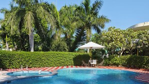 Una piscina con borde rojo y blanco a cuadros, rodeada de abundante follaje y palmeras.