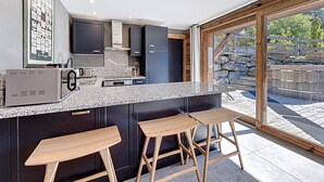 Una cocina moderna con armarios oscuros, encimera de granito y un ventanal con vistas a una pared de piedra y vegetación.