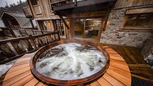 Un jacuzzi rodeado por una terraza de madera y muros de piedra.
