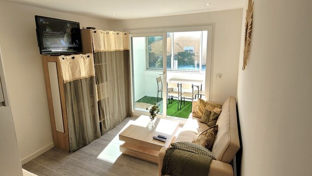 A modern living room with a flat-screen TV, a sofa, a coffee table, and a sliding glass door leading to a patio.