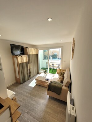 A modern living room with a flat-screen TV, a sofa, a coffee table, and a sliding glass door leading to a patio.