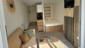 A compact living space with a sofa, a coffee table, a bed, and a television.