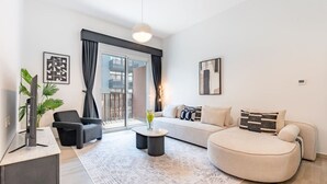 A modern living room with a sofa, armchair, coffee table, and a TV on a stand. - Contemporary 1Bedroom Escape in Eaton Place (Dubai)