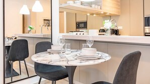 A modern kitchen with a marble island, pendant lighting, and a dining area with a round table and chairs. - Contemporary 1Bedroom Escape in Eaton Place (Dubai)