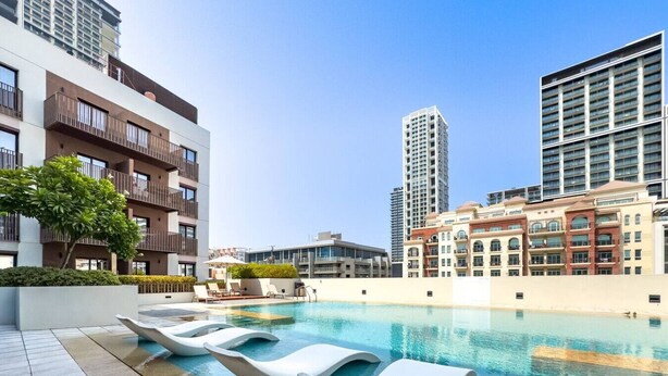 A rooftop pool with lounge chairs, modern buildings, and a clear sky. - Contemporary 1Bedroom Escape in Eaton Place (Dubai)