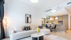 A modern living room with a sofa, coffee table, and a dining area with chairs. - Contemporary 1Bedroom Escape in Eaton Place (Dubai)