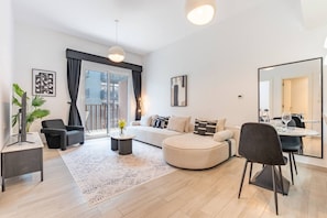 A modern living room with a sofa, armchairs, a coffee table, a dining table with chairs, a large mirror, and a balcony with a view. - Contemporary 1Bedroom Escape in Eaton Place (Dubai)