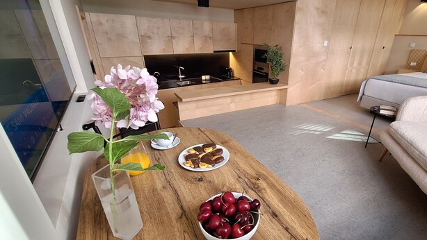 A modern living room with a wooden coffee table, a bowl of cherries, a plate of chocolate-covered snacks, and a potted plant. - Anémona Apartments GR FL – Your Home in Matosinhos, Where City Meets the Sea (Matosinhos)