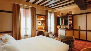 A hotel room with a large bed, wooden ceiling beams, a desk with a chair, and a bookshelf.