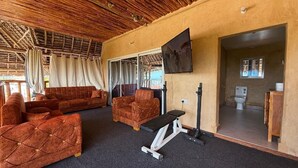 Een kamer met rieten dak, een zithoek, een bank, een televisie en uitzicht op de omgeving.