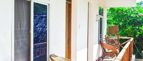 A balcony with wicker furniture, a door, and a view of greenery.