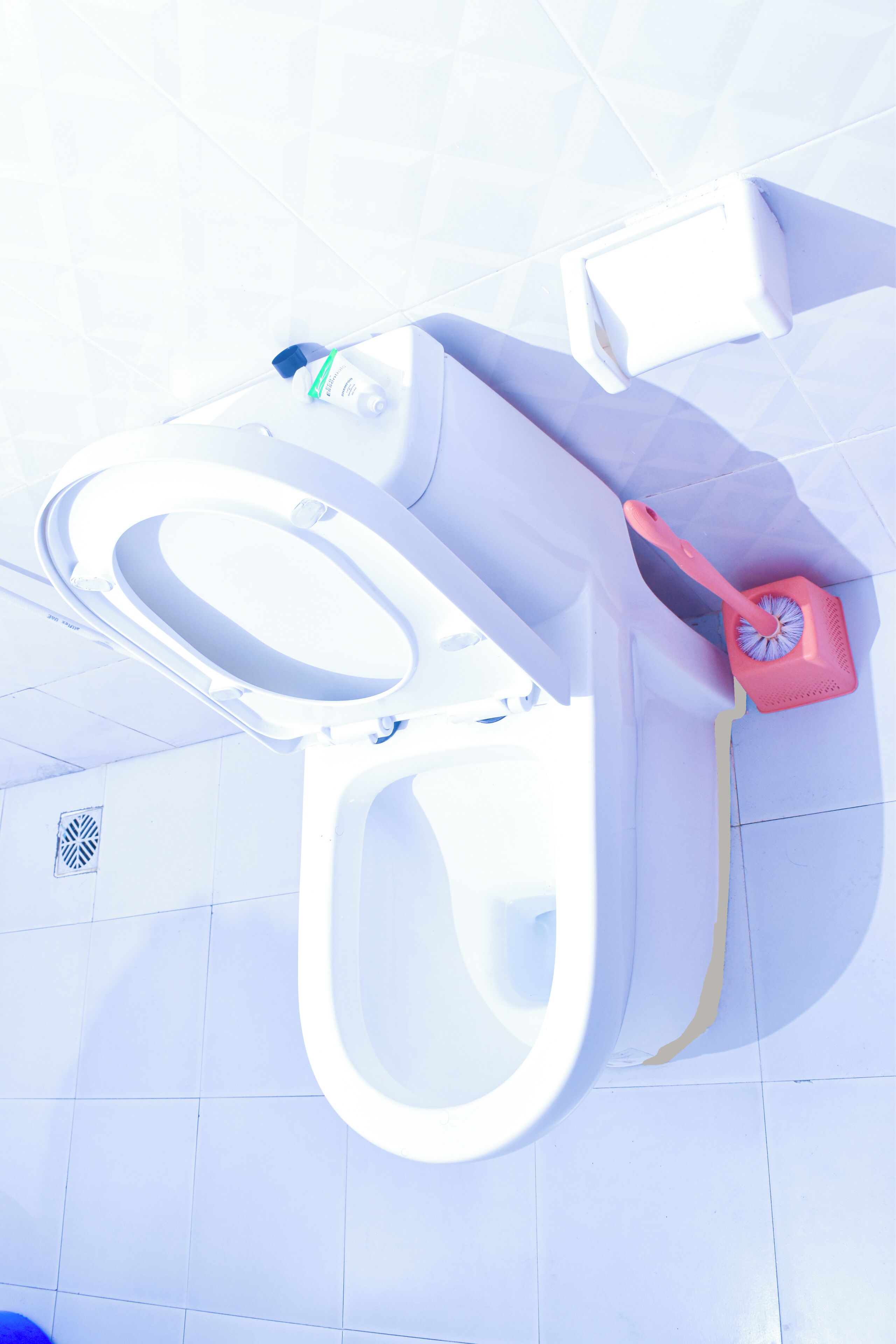 A toilet with a bidet attachment, a hand dryer, and a trash bin.