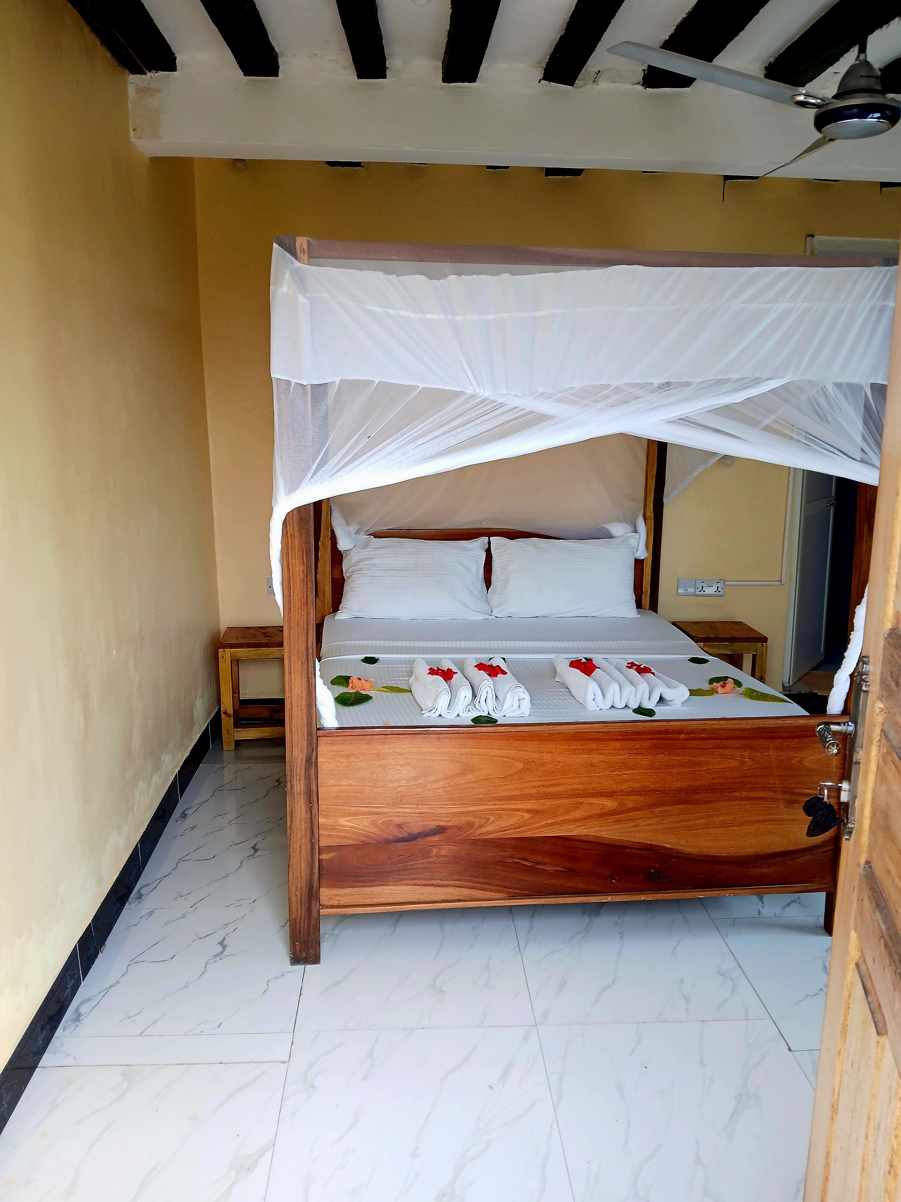 Een bed met houten frame, witte beddengoed en een klamboe.