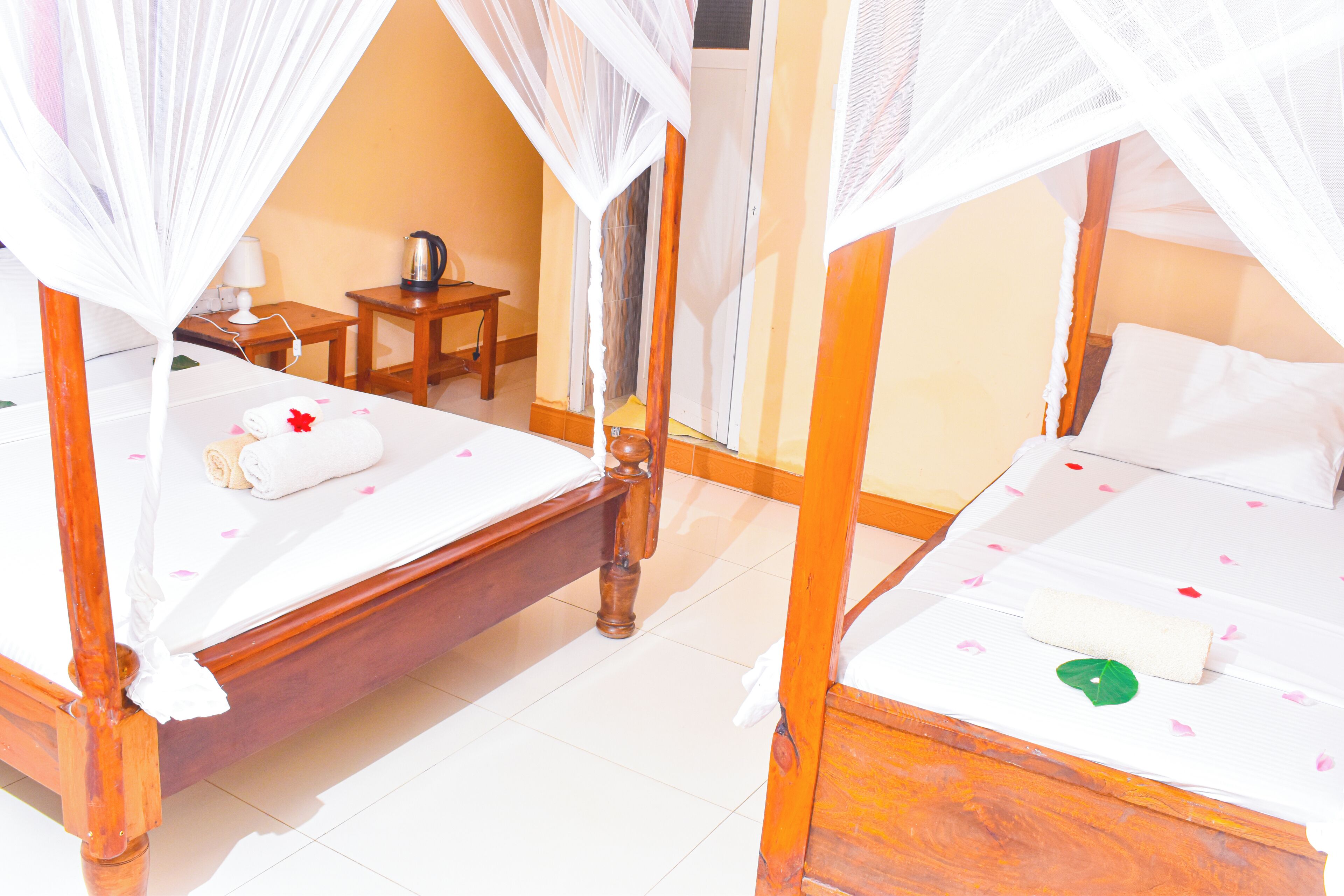 A room with two wooden beds, each with a canopy, a small table, and a chair.