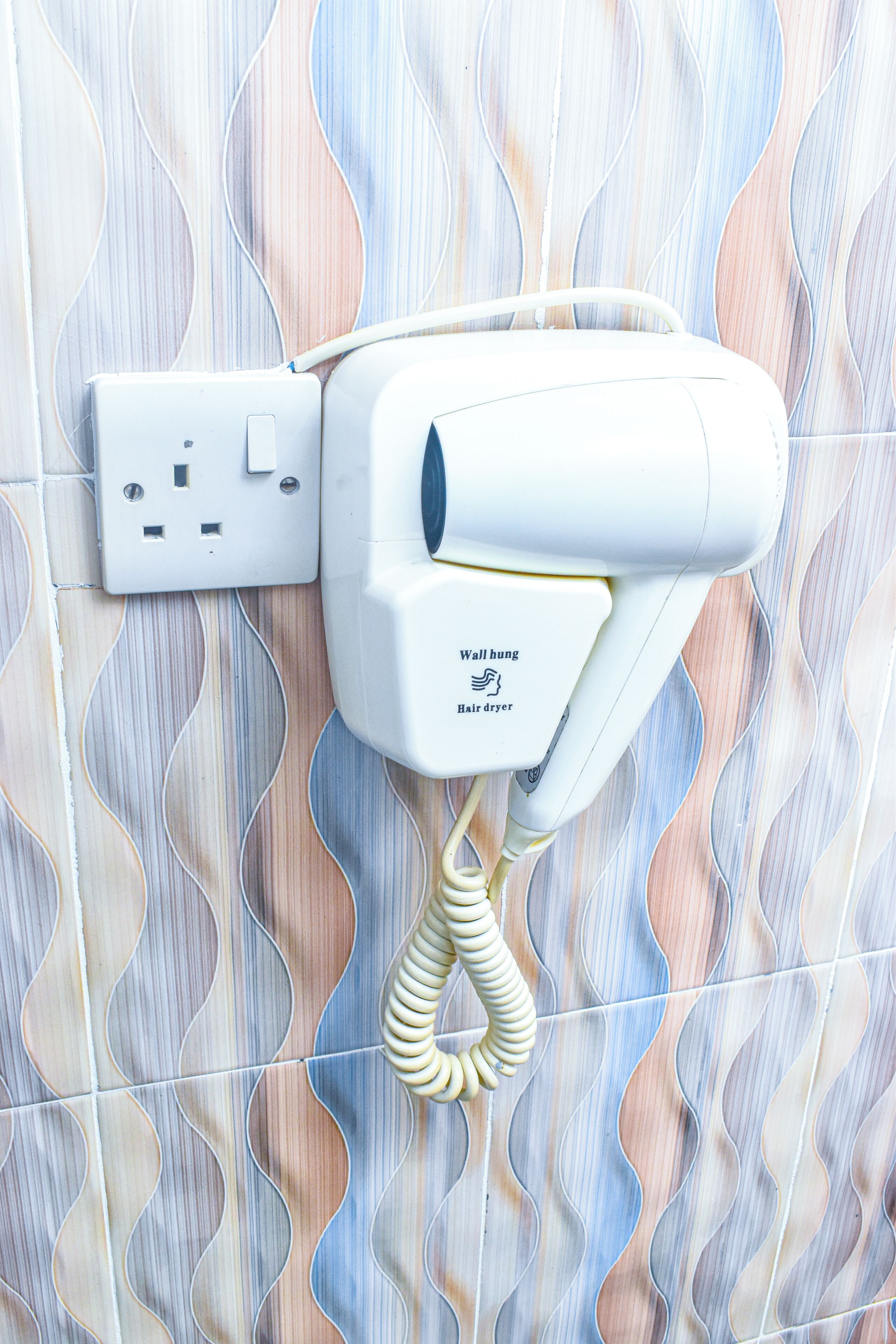 Een haardroger bevestigd aan een betegelde muur met een stopcontact.