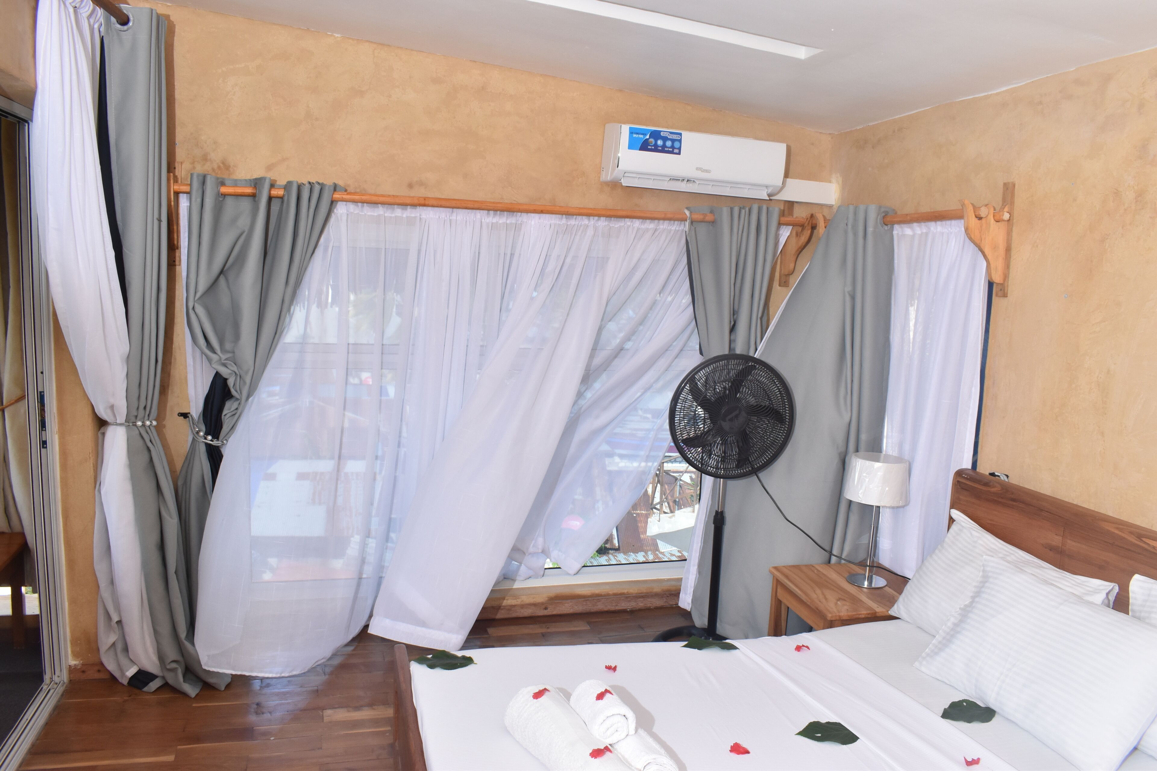 Ein Hotelzimmer mit einem Bett, einem Nachttisch mit Lampe, einer Klimaanlage und einem Vorhangfenster.