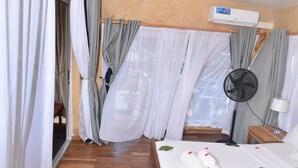 Een hotelkamer met een bed, een ventilator, een nachtkastje en een raam met gordijnen.