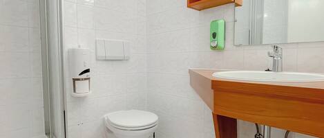 Un baño moderno con cabina de ducha de vidrio, inodoro, lavabo con tocador de madera y espejo sobre el lavabo.