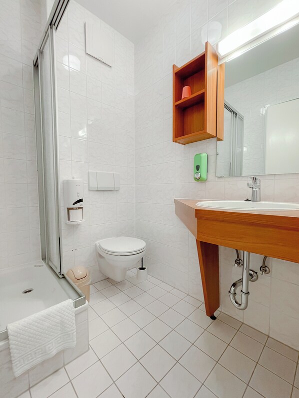 Un baño moderno con cabina de ducha de vidrio, inodoro, lavabo con tocador de madera y espejo sobre el lavabo.