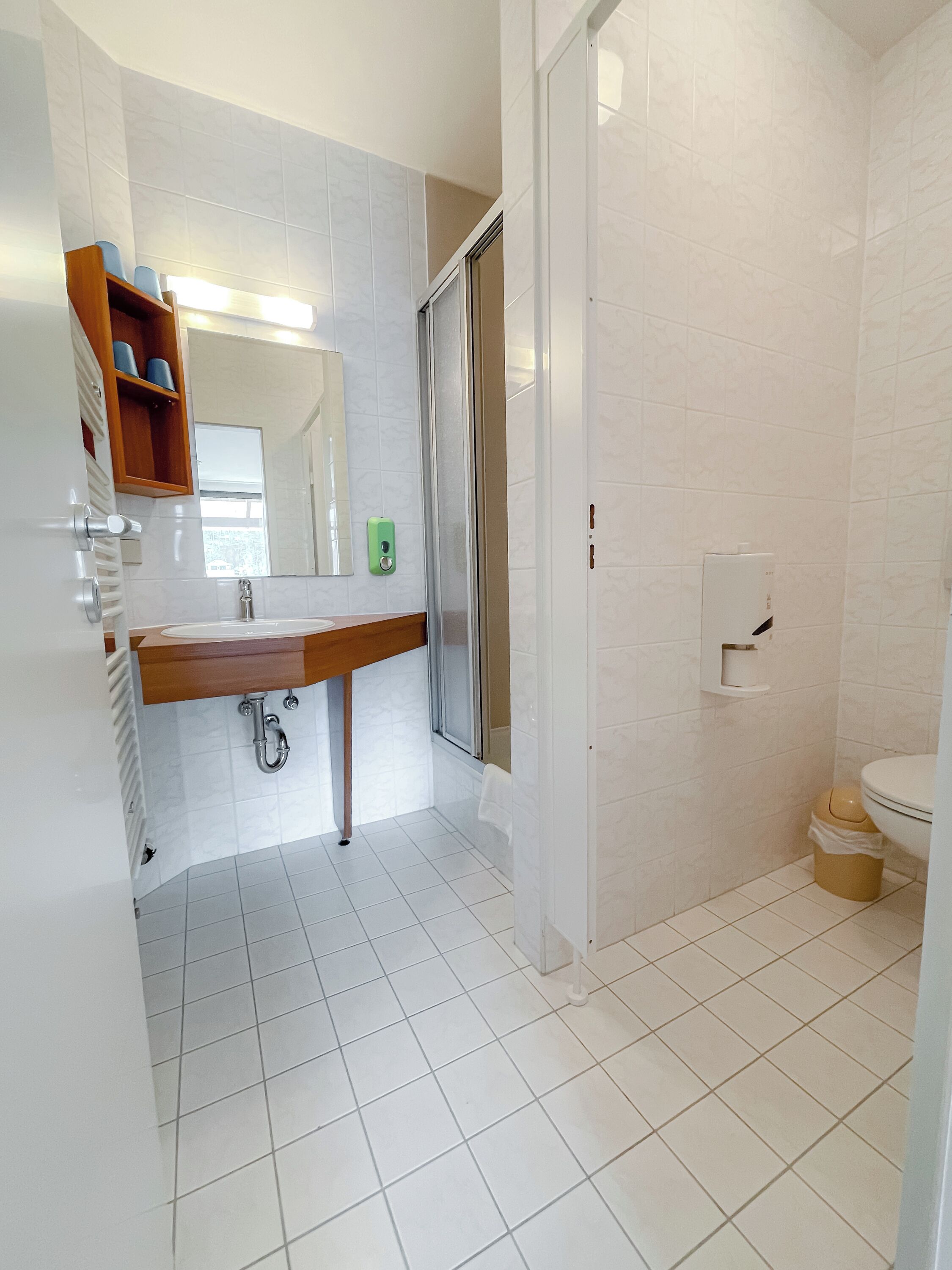 A bathroom with a white tiled floor, a wooden vanity with a sink, a mirror, and a shower enclosure.