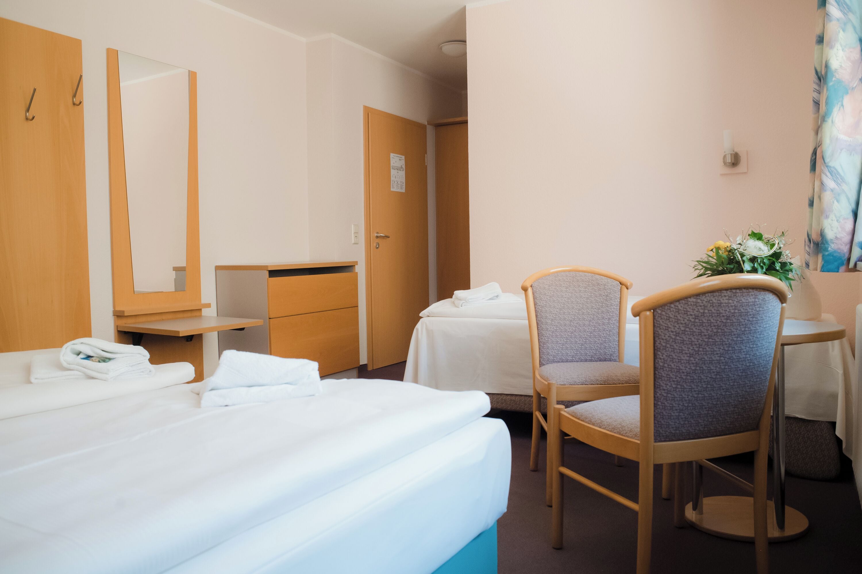A hotel room with a bed, a chair, a desk, a mirror, and a door.