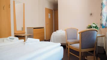 Ein Hotelzimmer mit Bett, Sessel, Schreibtisch, Spiegel und Tür.