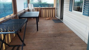 A covered patio with a table and chairs, a cat lying on the floor, and a sliding glass door leading to a house.