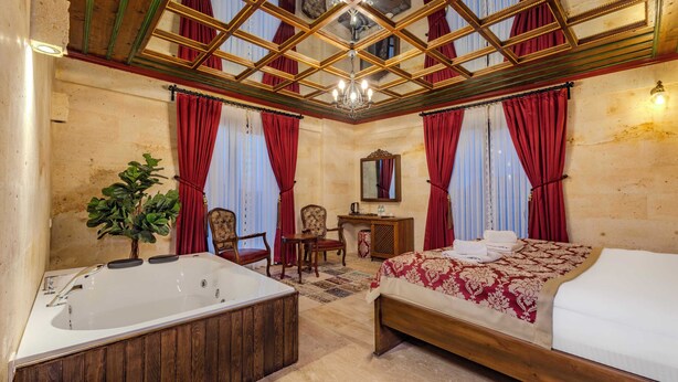 A spacious hotel room with a large bed, a separate bathroom with a bathtub, a wooden vanity, and a chandelier.