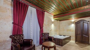 A room with a wooden ceiling, a large bathtub, two leather armchairs, a round table, and a wooden wardrobe.