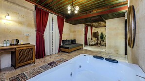 A room with a large white bathtub, a wooden desk with a kettle, and a sofa with red curtains.