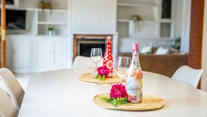 Una mesa de comedor con una botella de Don Simon Sangría Premium, dos vasos y una flor decorativa sobre una base tejida.