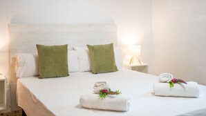Una cama bien hecha con dos almohadas, dos toallas enrolladas con flores y una mesita de noche con una lámpara.