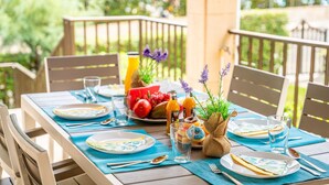 Mesa de comedor exterior con platos, cubiertos y una cesta de frutas.
