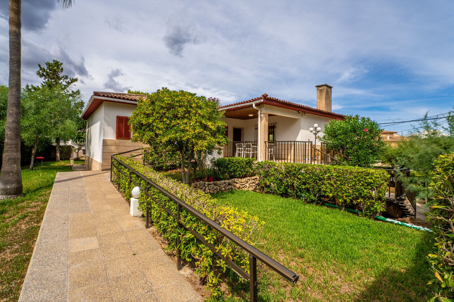 A house with a paved pathway leading to a covered porch with outdoor seating.