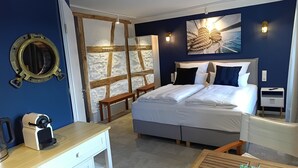 Ein Hotelzimmer mit einem Bett, einem Schreibtisch, einem Stuhl, einem kleinen Tisch, einem Spiegel, einer Wand mit Struktur und einem Gemälde.