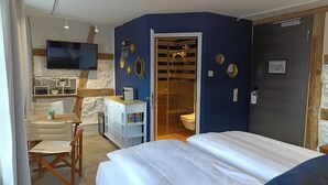 Ein Hotelzimmer mit einem Bett, einem Schreibtisch mit Stuhl, einem Fernseher, einem Badezimmer mit Dusche und einer Tür mit Schloss.