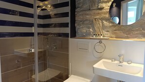 Ein modernes Badezimmer mit einer gläsernen Dusche, einem weißen Waschbecken und einer Wand mit Steinverkleidung.